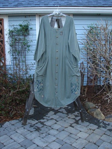 Alt text: "2000 NWT 4 Leaf Clover Dress: Green dress with laced backing, squared off neckline, oversized wrap front pockets, and flared hemline. Made from mid-weight organic cotton. Features leaf window theme paint and Blue Fish signature buttons."
