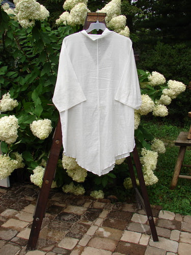 Image alt text: Barclay Batiste Flutter Tunic Top, a white shirt on a rack, featuring a V neckline, rear flutter collar, and horizontally pinched three-quarter length sleeves. Size 3.