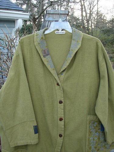 A green Barclay Patched Flannel Frolic Jacket on a swinger. Sweet roll over patched and painted neckline, contrasting lower sleeves, and four unique buttons. Just sooo cozy and swings just great!