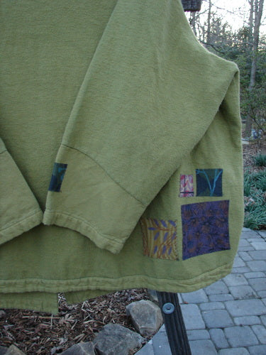 A green jacket with patchwork design, featuring a ribbed corded outer and unique buttons. This Barclay Patched Flannel Frolic Jacket in Green Seed is from a Winter Collection. Cozy and stylish, it has a widening hemline and sweet painted patches. Size 2.