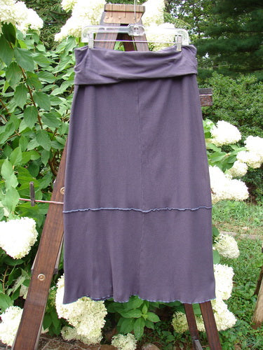 Barclay Thermal Fold Over Pencil Panel Skirt, a purple skirt on a clothes rack. Made from Organic Cotton Thermal, with a fold over waistline panel and a longer straighter fall. Exterior horizontal stitchery and a little full circumference lettuce edge. Panel measures 32 by 8 stretchy inches. Hips measure 44 and full length is 40 inches.