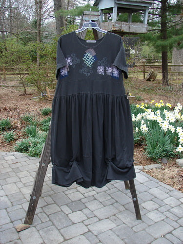 1996 Constellation Dress: A black dress with a patchwork design on it. Features adjustable hemline with loops and buttons, rear buttons, and a front detachable painted pocket. Size 2.