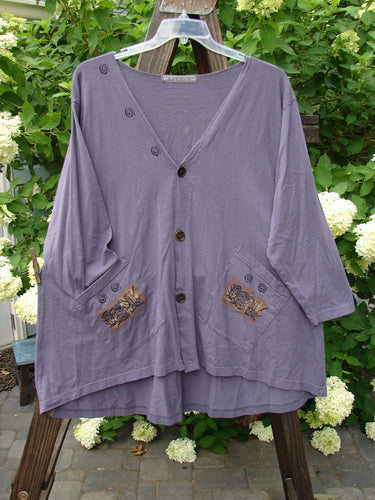 1996 Triangle Cardigan Garden Bug Purple Martin OSFA: A purple shirt with pockets on a wooden rack. A close-up of a white flower.