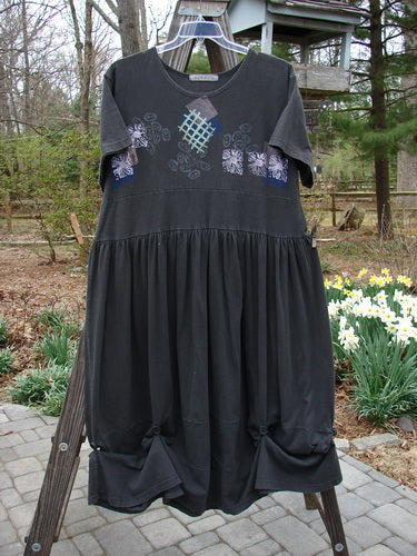 1996 Constellation Dress Garden Path Storm Size 2: A black dress with a patterned hemline, rear buttons, and a detachable painted pocket. Features a gathered full skirt and a deeper scooped neckline.