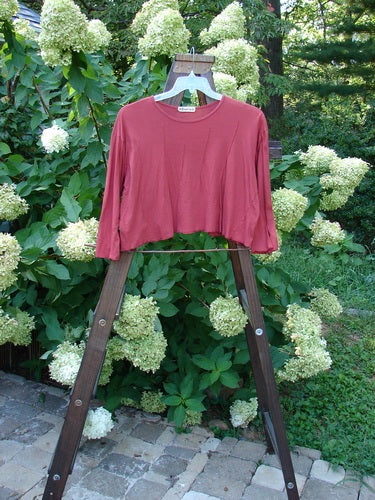 A red Barclay Batiste Pinch Crop Top, size 1, on a wooden stand. Crop wide shape with vertical pinch accents and three-quarter length sleeves. Shallow neckline and widening lower hem. Unpainted.