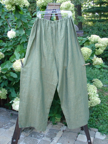 A pair of 2000 Cross Dye Linen Map Pocket Pants in Meadow, Size 2, on a wooden pole. Features include a full elastic waist, deep cargo pockets, and a longer length. Perfect for fishers who love the softness of superior linens.