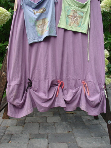 1997 Salt Water Taffy Jumper, a purple dress with a pink and green shirt on a wooden stand. Versatile design with rippie accents, front and back pockets, textured buttons, and ocean summer theme paint. Size 2.
