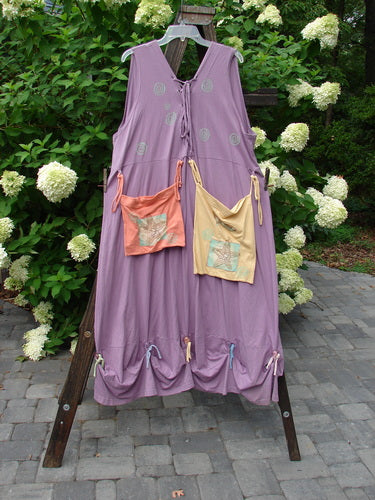 1997 Salt Water Taffy Jumper, a purple dress on a wooden stand. Versatile design with rippie accents, tie-on front and back pockets, and clear textured buttons. Perfect for summer with ocean-themed paint. Size 2.