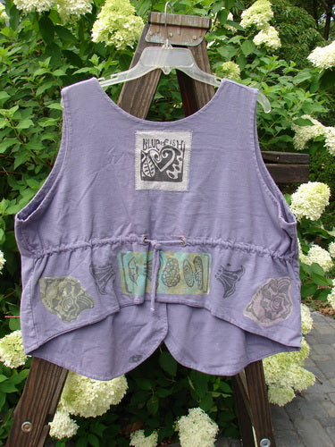 1993 The Vest Mushroom Garden Periwinkle Size 1: A purple vest with designs and a logo on it. Vintage, oversized, and made from double-layered cotton. Tuxedo-style front tails, wider shape, and crop draw corded back. Features a heart signature 93 patch and mushroom garden theme paint.