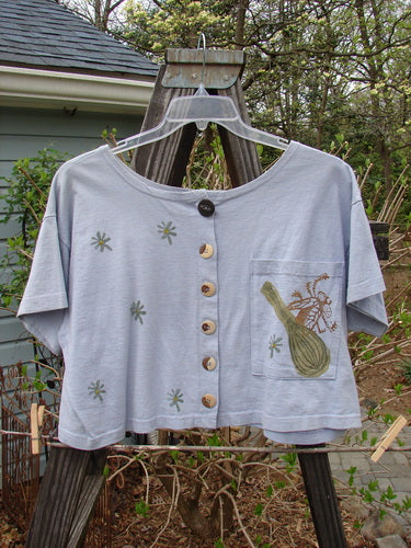 1994 Song Top Vintage Kitchen Garden Lavender Size 1: A shirt on a swinger with a design on it, featuring a drawing of a bee and a flower. The shirt has a wide boxy shape, a shallow neckline, and a painted breast pocket.