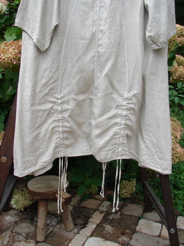 Barclay NWT Linen Shimmer Venetian Tunic Dress Unpainted Sand Shell Size 2: A white shirt on a chair, showcasing a generous elongating shape, wider hip and hemline sweep, and softly rounded bottom V-shaped neckline.