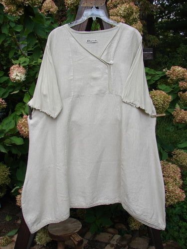 Barclay Linen Lace Blooming Tunic Dress Unpainted Wheat Size 2: A white dress on a clothes rack with lace trim on the hem and three-quarter scallop-edged sleeves.