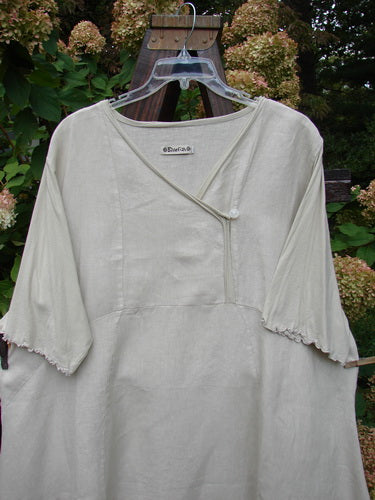 Barclay Linen Lace Blooming Tunic Dress Unpainted Wheat Size 2: A white shirt on a swinger with a cross over neckline, lace trim on the hem, and three-quarter scallop-edged sleeves.