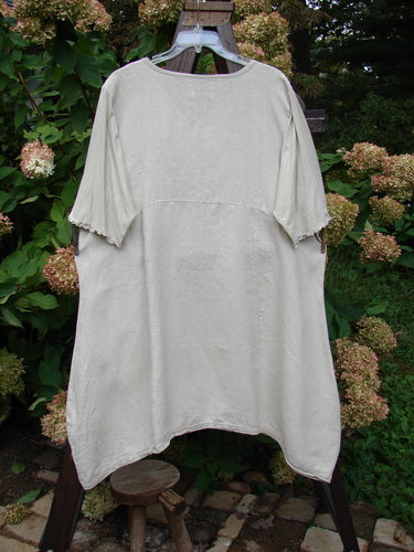 Image alt text: Barclay Linen Lace Blooming Tunic Dress on clothes rack, with cross over neckline, empire waist seam, and overlay lace trim on hem.