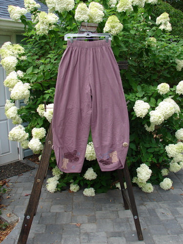 1996 Boulevard Pant Old Car Travel Laurel Size 1: A pair of pants on a rack with overlapping painted cuffs and cloth covered buttons.