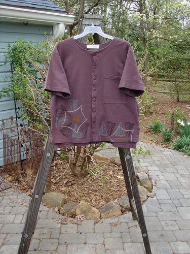 Image alt text: 1998 Camp Shirt Triangular Star Madeira Size 1: Purple shirt with a design on it, on a wooden stand, in outdoor setting with trees and plants.