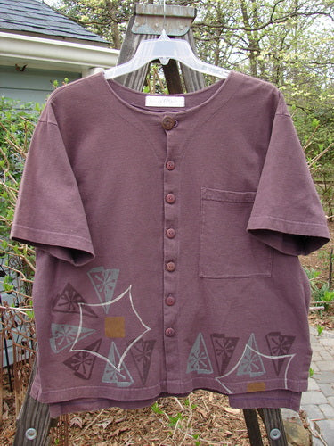 A 1998 Camp Shirt Triangular Star Madeira Size 1: a purple shirt with a design on it, made from organic cotton. Features include a straighter boxier shape, vented hemline, Blue Fish patch, oversized front breast pocket, and shirt tail like hem. Bust 50, waist 50, hips 50, front length 26, back length 28 inches.