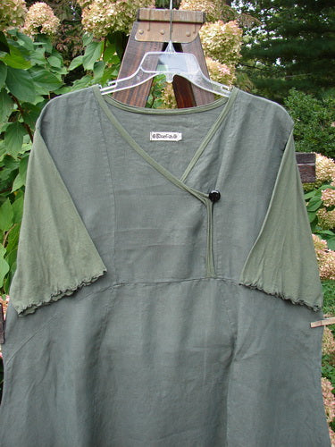 Barclay Linen Lace Blooming Tunic Dress Unpainted Army Size 2: A green shirt on a swinger with a cross over neckline, lace trim on the hem, and three-quarter scallop-edged sleeves.