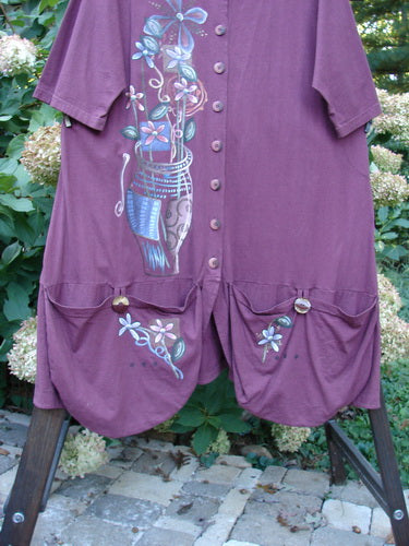 Barclay Short Penny Dress Garden Show Red Plum Size 2: A purple dress with a painting of a garden show theme. Features include a rounded neckline, painted pockets, and a flowing paneled lower swing.