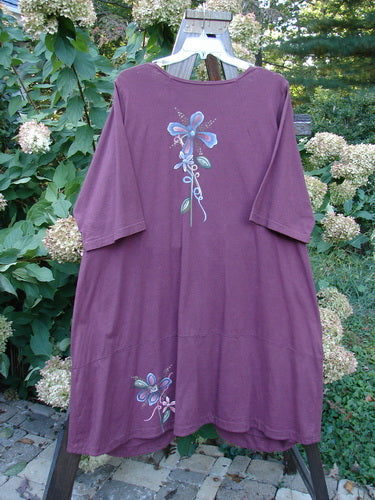 A purple dress with a flower design, featuring a sweet rounded neckline, longer widening shape, and painted garden show theme. It has two front bottom heavy painted pockets and a paneled lower swing for a super drape and flow. Size 2.