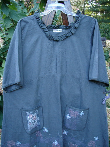 Barclay Linen Duet Sunrise Dress in Stormy Grey Size 2, featuring a ruffled neckline, empire seam, and floral-appliquéd pockets, hangs outdoors, embodying Bluefishfinder.com's vintage-inspired, artistic style.