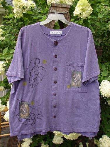 1998 Camp Shirt Falling Leaf Modena Size 2: A purple shirt with a leaf design, featuring a straighter boxier shape, vented hemline, and oversized front pocket.