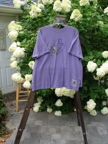 1998 Camp Shirt Falling Leaf Modena Size 2: A purple shirt with a leaf design on a wooden rack. Straight, boxy shape with a vented hemline and oversized front pocket.