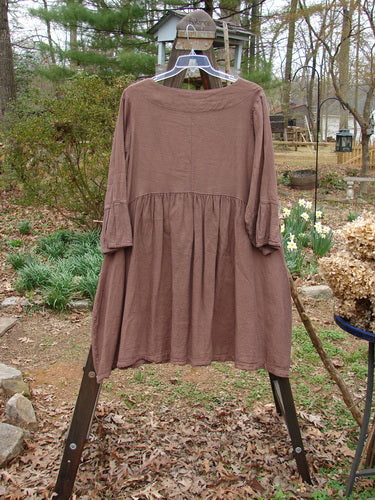 Image alt text: Barclay Linen Adras Uptown Jacket Unpainted Redwood Size 0 - A brown dress on a rack with sectional triangular panels, pleated lower sleeves and hemline, and double exterior drop front pockets.