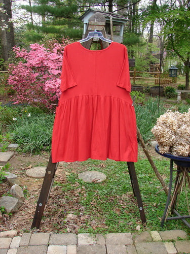 Barclay Studio Boxcar Dress Unpainted Real Red Size 1: A red dress on a rack with a rounded neckline, curved waist seam, and flared lower flounce. Features two side pockets.