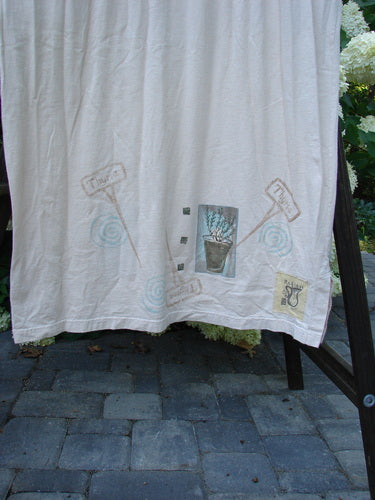 A white towel with drawings, a white shower curtain with a plant drawing, a white cloth with a logo, a stone walkway, and a close-up of a white curtain.