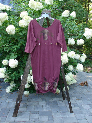 A 1993 Deep Neck Button Dress in Woodberry with Roman Strings. Made from Cotton Jersey, this dress features a deep and wide neckline, a lower tapering shape, and three vertical bottom interior draw cords. The continuous empire seam button accent adds a unique touch. Bust 46, Waist 44, Hips 44, Taper 46, Length 48.