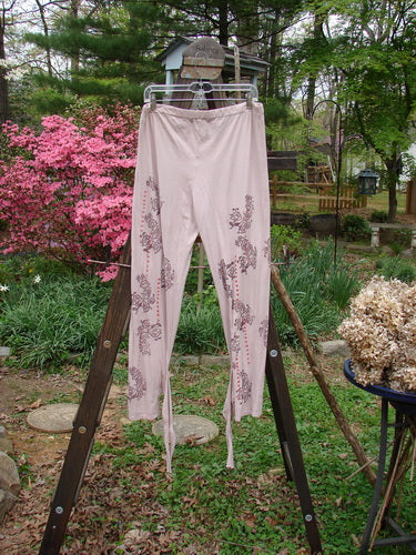 Barclay NWT Batiste Wrap Layering Pant Legging Flower Peach Bisque Size 2: A pair of pants on a rack with a design on it, featuring a trailing curl vine theme.