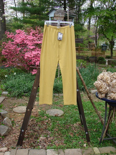 Barclay NWT Cotton Lycra Bally Layering Legging Unpainted Oil Yellow Size 2: A pair of pants on a rack, featuring a longer, slightly narrowing lower leg. Made from medium weight cotton lycra, these pants have a soft and forgiving feel.