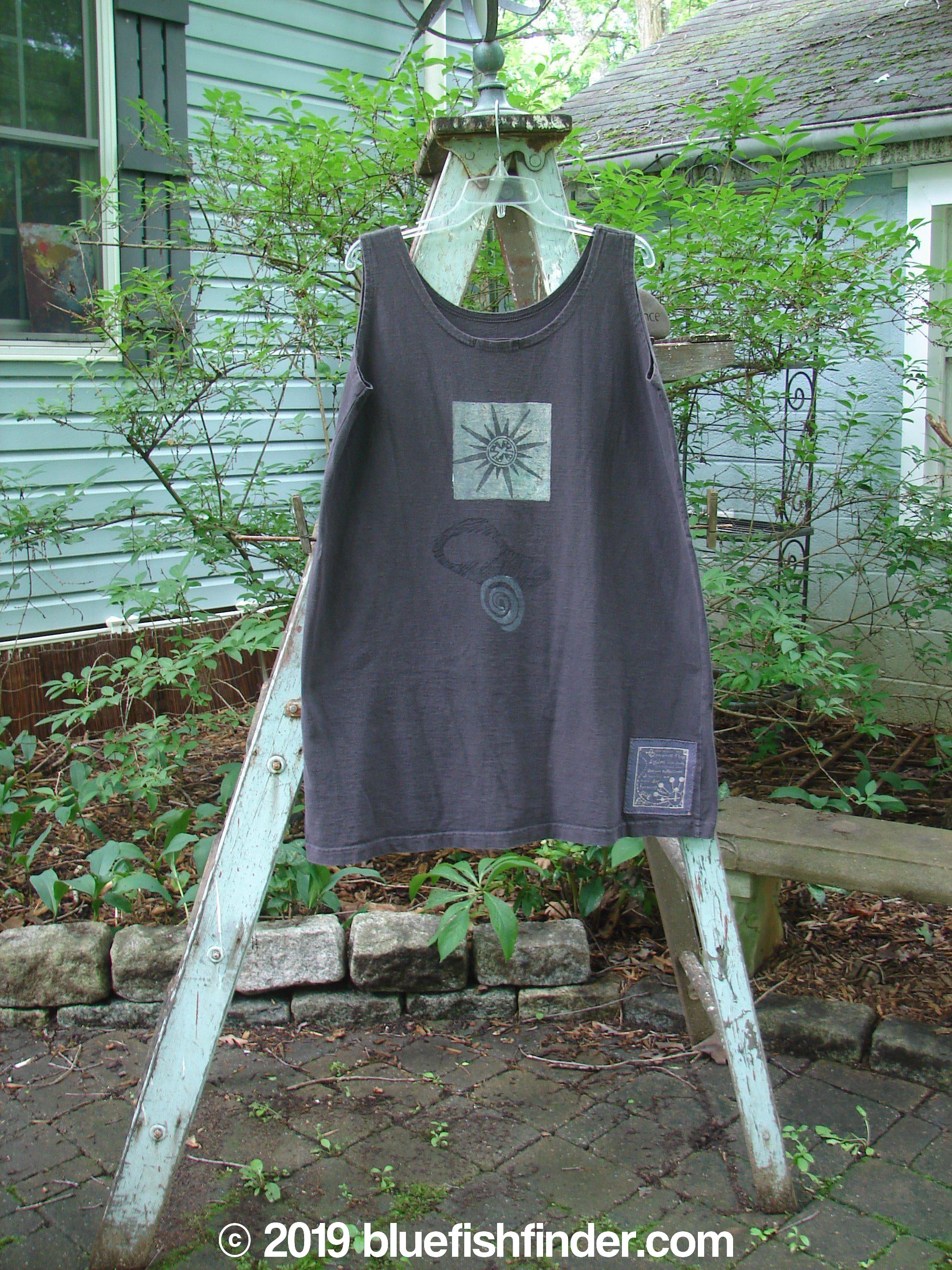 1995 Sun Glint Tank Atom Briquette OSFA: A shirt on a clothes rack, featuring a black and white drawing of a sun. Perfect condition, made from organic cotton. Generously sized tank with a slight reverse A-line shape, scooped neckline, and signature Blue Fish patch. Ideal for hot summer days. Bust 56, waist 54, hips 54, length 34 inches.