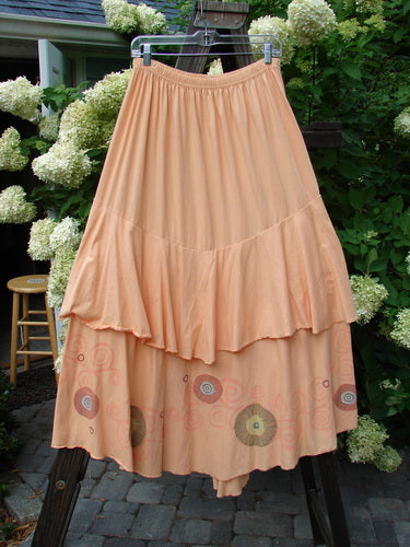 Barclay Two Story Skirt Bubbles Sherbet Size 2: A peach skirt with fluttering edges, hanging on a clothesline. Organic cotton, dual-layered, and featuring a bubble theme.