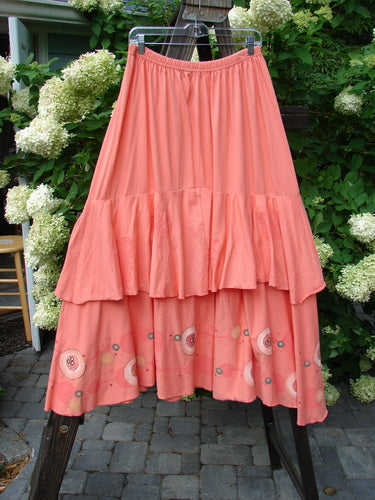 Barclay Two Story Skirt Bubbles Tangerine Size 2: A pink skirt with ruffles and a full elastic waistline, made from organic cotton. Features a drop hip seam, flutter-like edges, and a large lower sweep.