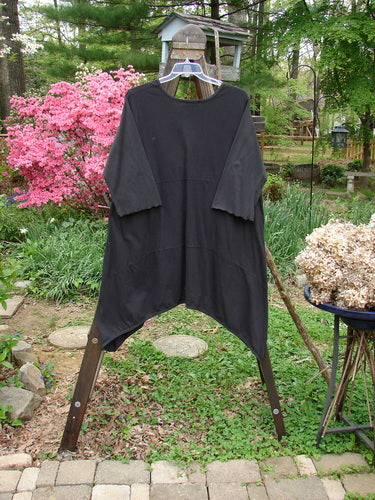 Barclay Vector Tunic Dress Unpainted Black Size 2: A black shirt on a clothes rack, with a close-up of a metal object and a pile of white flowers.
