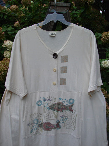 Barclay Tunnel Pocket Pull Over Dress Fish Natural Size 2: A white shirt with a fish painted on it. Features a drop tunnel kangaroo pocket.