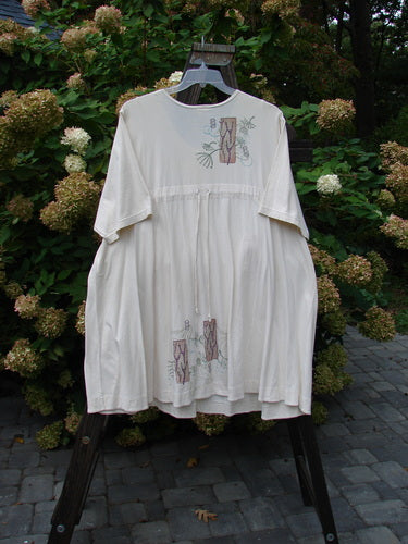 Image alt text: Barclay Tunnel Pocket Pull Over Dress Fish Natural Size 2 - A white dress with a fish-themed painting, featuring a drop tunnel kangaroo pocket and a widening lower sweep.