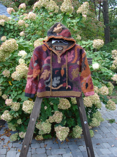 A Tara Handknit Kids Hooded Pocket Pullover in Size Large. Handcrafted by the Hot Knots Sisters, this vintage beauty features colorful patterns, a cozy ribbed neckline, and a drawcord hoodie accent. Complete with oversized metal buttons and a kangaroo cargo pocket, this luxurious piece promises to be your favorite this winter!