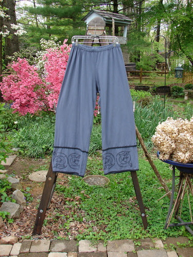 A pair of Barclay Cotton Lycra Tic Tac Toe Pants in Blue Dusk, size 2, on a rack in a garden. Longer inseam, slenderizing fall, contrasting lettuce lower edgings, and a snappy lower flair. Waist fully relaxed: 30, waist fully extended: 62, inseam: 28, length: 40 inches.