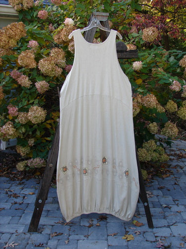 2000 Cotton Hemp Libby Jumper Bright Sun Dove Size 2: A white dress with a floral design on a wooden stand, showcasing a downward scooped waistline, 2 side pockets, and a bubbled shape.