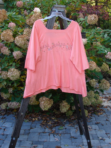 Image alt text: Barclay Be There Top Flower Power Tangerine Size 2: A pink shirt with a flower design, featuring a squared double paneled deeper neckline, empire waist seam, wide full pleats, and a forever skirt flair.