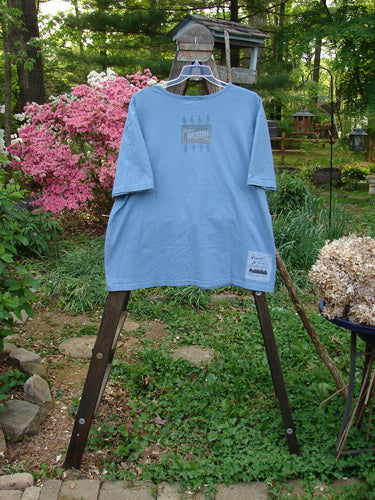 2000 Short Sleeved Tee Greetings Doylestown Bluestone Size 1: A blue shirt with a rolled neckline and drop shoulders, featuring a Blue Fish patch and Doylestown theme paint.