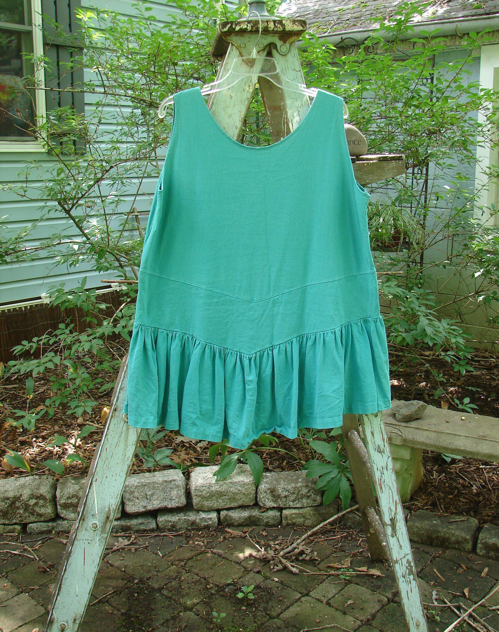 Image alt text: "1990 Button Tier Top in Turq, a blue dress with a gathered flounce and ruffled hemline on a clothes rack"