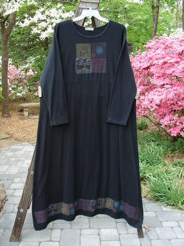 A black dress on a clothes rack, featuring a long black robe with a face on it, a pink bush, a stone walkway, and a fabric close-up. The Barclay Hemp Cotton Curved A Line Dress is from a Fall Collection in Black, with a wide A-line shape, cozy sleeves, and vintage theme paint along the hem. Bust 52, Waist 56, Hips 58, Sweep 90, Length 57 Inches.