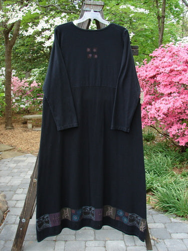 A black dress on a clothes rack, featuring a curved A-line shape and vintage theme paint along the hem. Made from medium weight hemp cotton, this Barclay Hemp Cotton Curved A Line Dress in size 2 is perfect for fall.