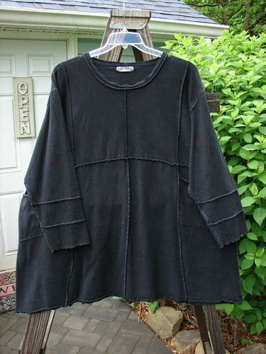 Image: A black shirt on a swinger. The shirt is part of the Barclay Hemp Cotton Dual Quadrant Dress in unpainted black, size 2. The dress features double quadrant exterior seams, a varying hemline, two front drop exterior pockets, and a piped and wavy neck and hemline. It has an A-line flare and wider curly edged three-quarter length sleeves. The dress is made from medium weight hemp cotton and is in perfect condition. The measurements are: Bust 58, Waist 60, Hips 62, Sweep 80, and Length 35 inches.