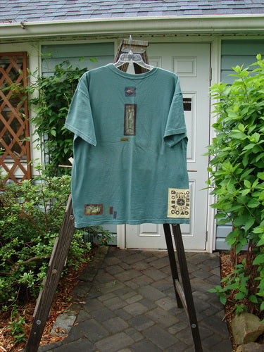 A vintage 1993 Short Sleeved Tee featuring a tractor design on a grey green background. Boxy shape, shorter sleeves, ribbed neckline, and Blue Fish patch. Bust 50, waist 50, length 30 inches.