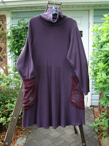 A medium-weight cotton thermal dress in cherry plum, featuring a turtleneck, oversized exterior drop pockets, varying hemline, exterior stitchery, and lettuce edges. The dress has a longer rounded A-line shape and is painted in the dried pod theme. Size 1.